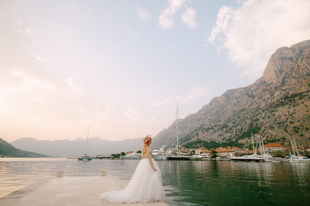 A bride in a delicate wreath of roses stands on a pier near Kotor in the Bay of Kotor