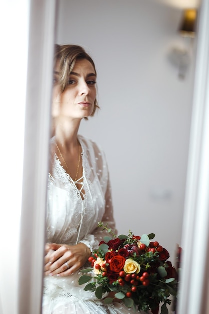 Photo bride in elegant white dress looking in mirror the bride smiles and poses in front of the mirror