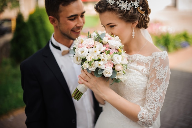 Bride enjoys the scent of a wedding bouquet, the groom stands beside smiling