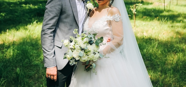 Bride and groom are hugging in the park Happy couple walking together Wedding day photo Love story Beautiful long sleeve dress Lace veil Stylish rustic bouquet