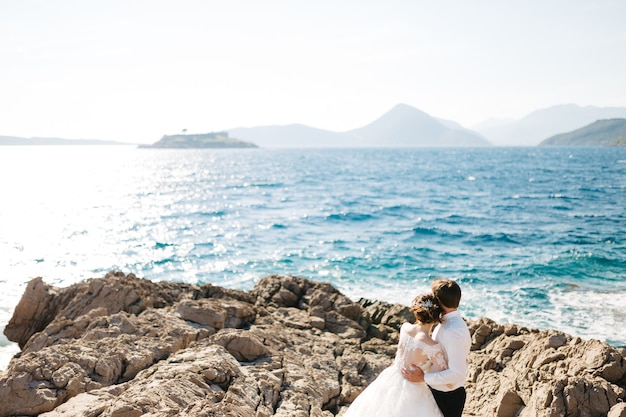 Bride and groom are hugging on the rocky beach of the Mamula island near Arza fortress. 