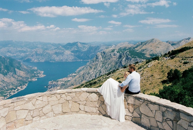 Bride and groom are sitting on an observation deck over the mountains