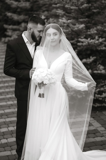 A bride and groom are standing on a brick walkway with the bride wearing a veil