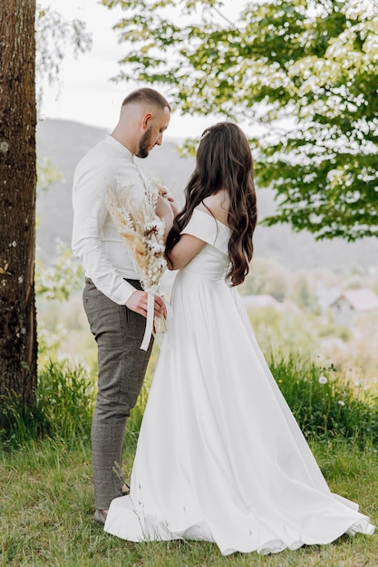 A bride and groom are standing in a field with a tree behind them