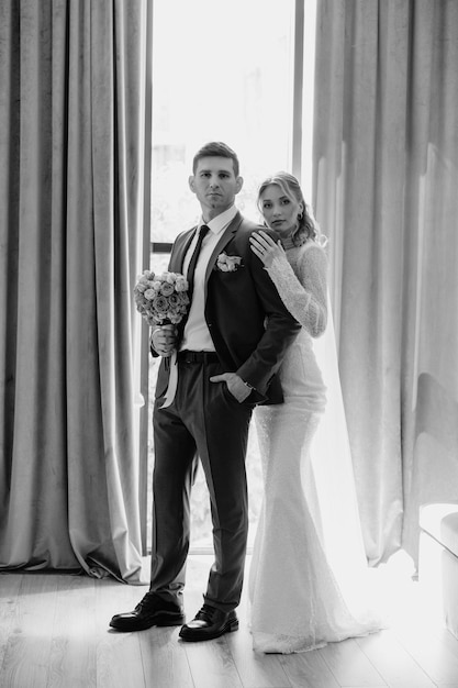 Photo a bride and groom are standing in front of a window