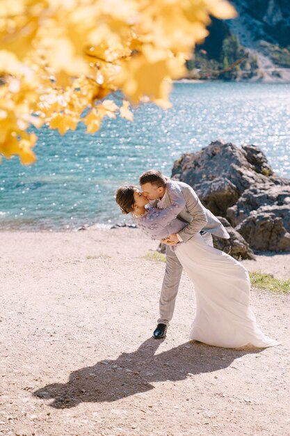 Bride and groom under an autumn tree with fiery yellow foliage at the lago di braies in italy