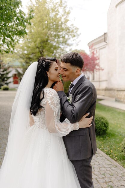 A bride and groom embrace on a path in front of a building.