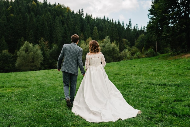 The bride and groom go back and walking holding hands on nature Back view Newlyweds of the outdoors Engagement Country