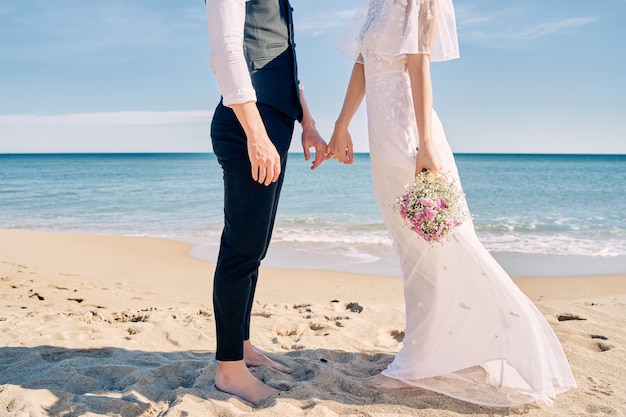 Bride and groom holding hands on the beach in wedding dresses