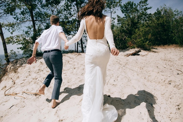 The bride and groom holding hands running on the sea beach The concept of love