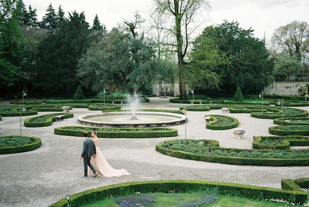 Bride and groom holding hands walk in the park near the fountain