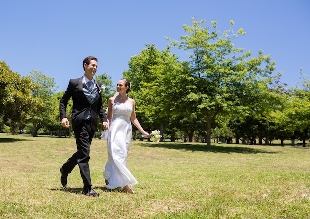 Bride and groom holding hands walking in park