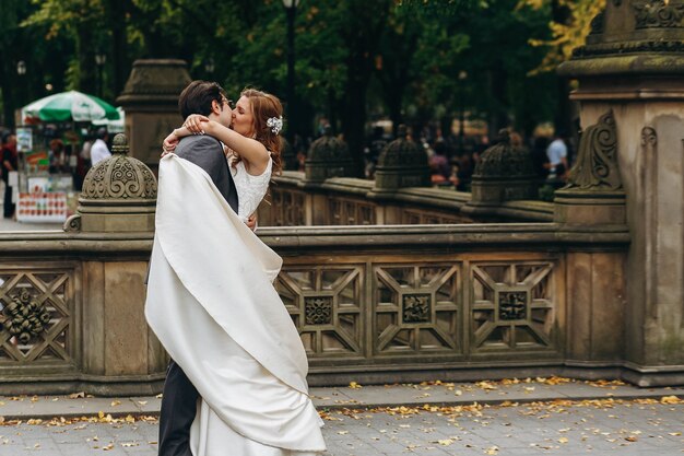 Photo bride and groom hug each other tender and kiss standing in the central park, new york