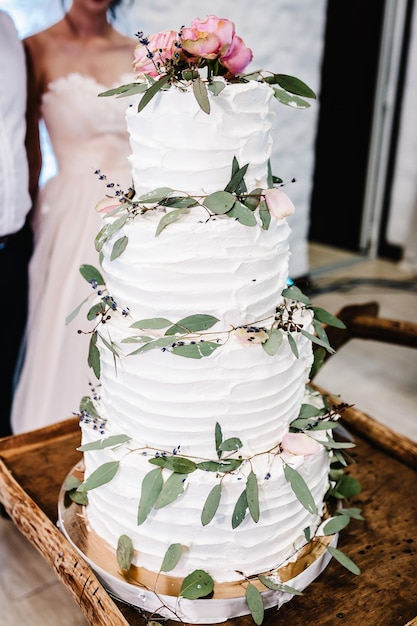 Bride and a groom is cutting their rustic wedding cake on wedding banquet Hands cut the white cake with delicate pink flowers