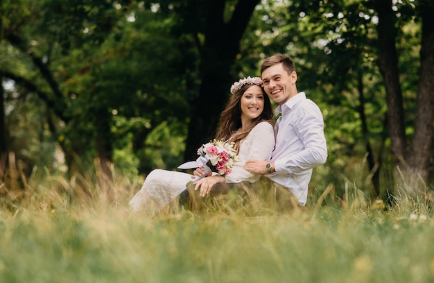 A bride and groom sit on a log in a field with trees in the background