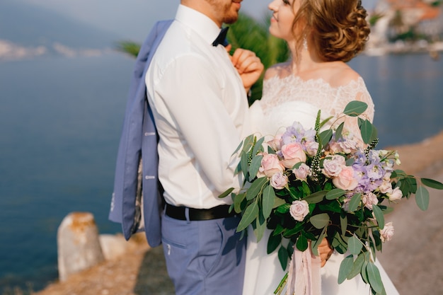 The bride and groom stand embracing on the pier the bride holds a bouquet in her hand