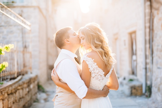 The bride and groom stand embracing on the streets of Perast, the groom kisses the bride on the