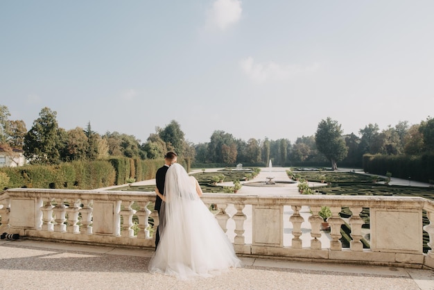 A bride and groom stand in a garden with a view of the palace of versailles in the background