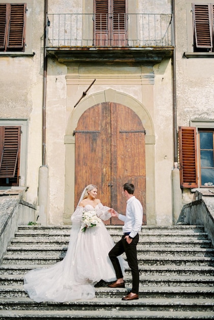 Bride and groom stand on the steps in front of the wooden door of an old building with shutters