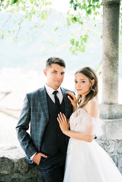 Bride and groom stand in a stone gazebo near the column