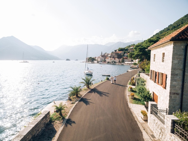 Bride and groom walk along the asphalt road along the coast of perast montenegro