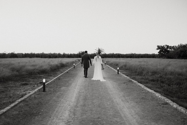 Photo a bride and groom walk down a dirt road.