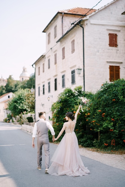 Bride and groom walk down the street past the old building back view