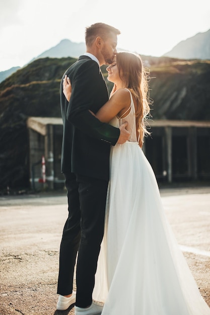 The bride and groom with stand hugging on mountains background the groom kisses the bride on the for