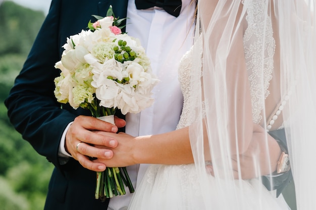 The bride and groom with a wedding bouquet, holding on hands and standing on wedding ceremony of the outdoor in the nature backyard.