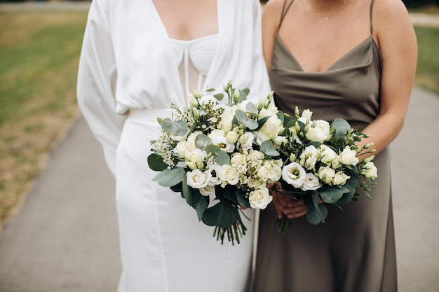 The bride and her friend are holding wedding bouquets of white roses