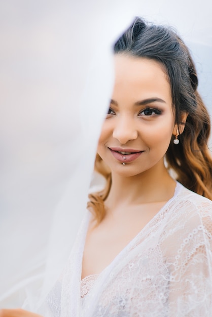 Bride in her underwear and a dressing gown with a veil walks on the beach