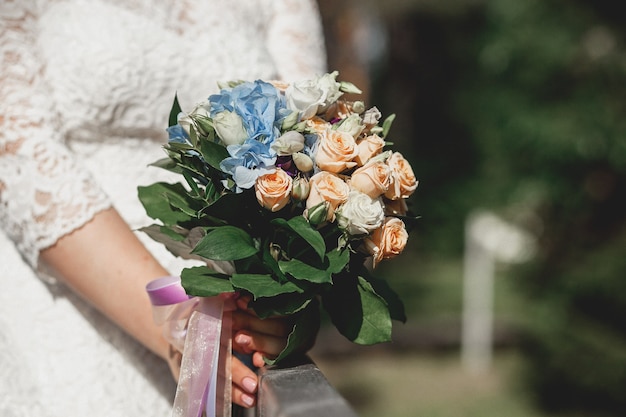 Bride holding bridal bouquet with white and creamy roses and blue flowers outdoors