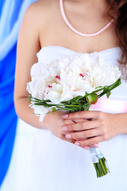 Bride holding wedding bouquet of white peonies closeup on color background