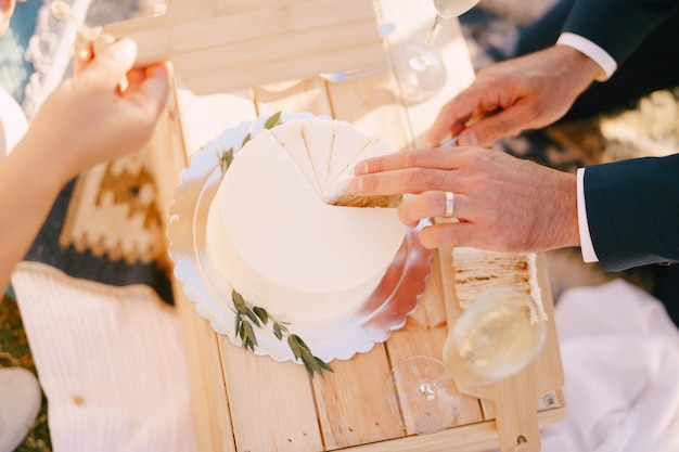 Bride holds out a wooden plank to groom who cuts a piece of the wedding cake cropped faceless