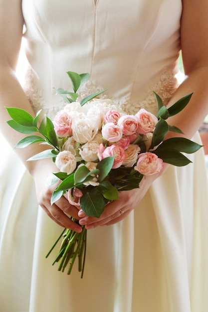 The bride holds a wedding bouquet of delicate white and pink roses, wedding accessories