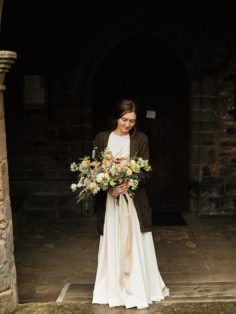 Bride holds wedding bouquet and looks down over cloudy day. close-up, big beautiful bouquet