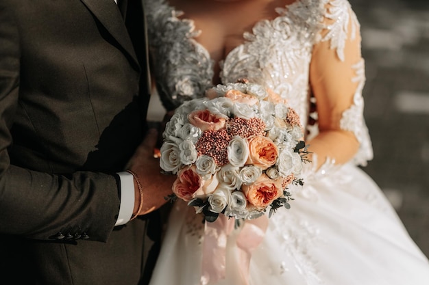 The bride is holding a beautiful wedding bouquet of pink flowers White wedding dress with beaded sleeves