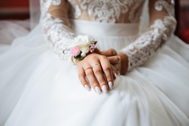 Bride is holding hands on knees Beautiful white manicure Engagement rings on fingers Wedding day details Elegant accessories