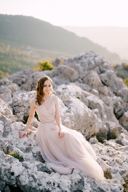 Bride in a long tulle dress sits on a rocky mountain