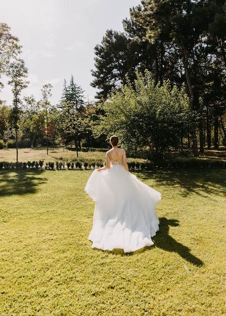 Bride in a long white dress running away on green grass