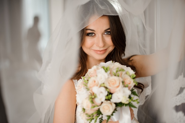 Bride morning preparation. Happy and smiling bride in a white veil with a wedding bouquet