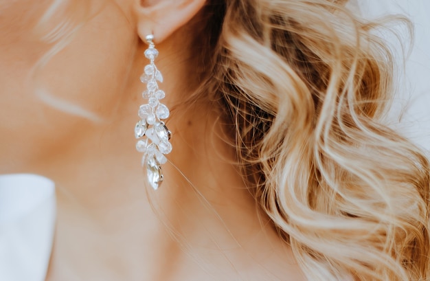 The bride puts on beautiful wedding earrings. Girl with hairstyle with curls wears jewelry accessories