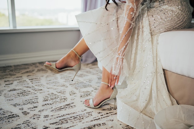 Bride putting on her stylish silver sandals