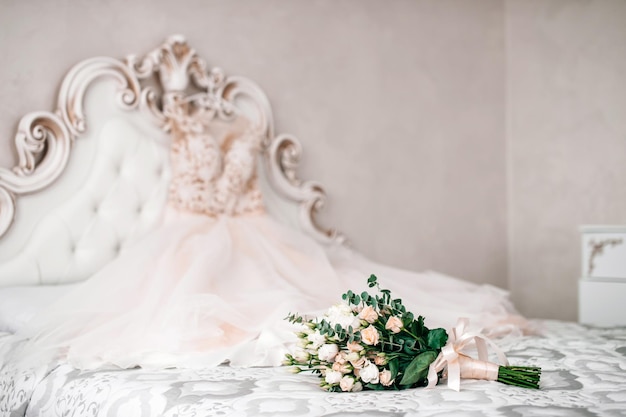 The bride's bouquet is lying on the bed with the wedding dress