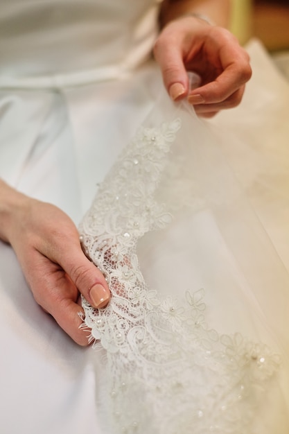 Bride's hand touching details of her wedding dress. Simple french manicure