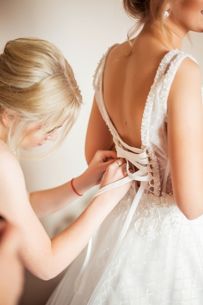 Bride's morning. Girlfriend helps put on a dress. Photo from the back. Lacing corset