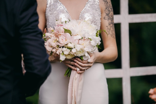 the bride in a soft pink dress holds a wedding bouquet in her hands at the ceremony.