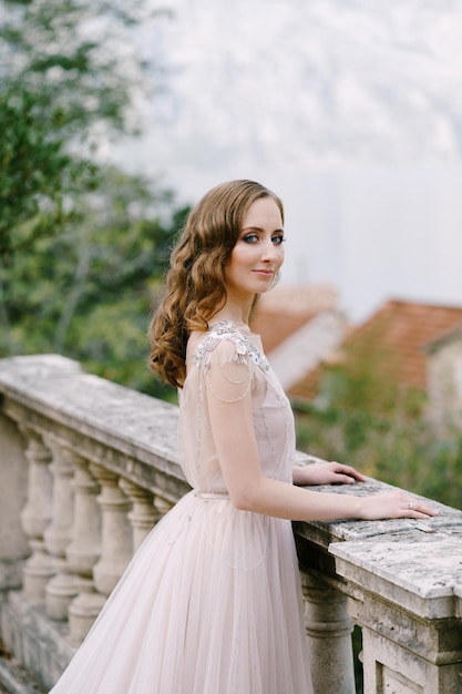 Bride stands on a stone terrace against the backdrop of the bay