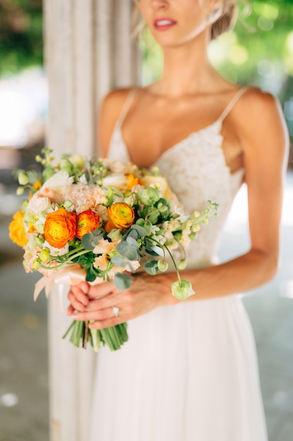 The bride stands among white columns braided with green vines and holds a wedding bouquet