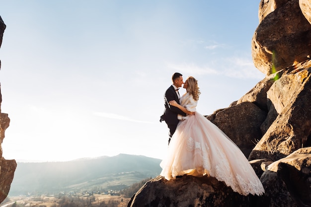 Bride in stylish dress with lace and groom in suit on a background of cliffs and mountains